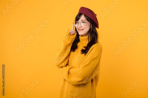 An attractive female model in a yellow sweater, red beret, and eyeglasses, looking thoughtful against a bright yellow backdrop.