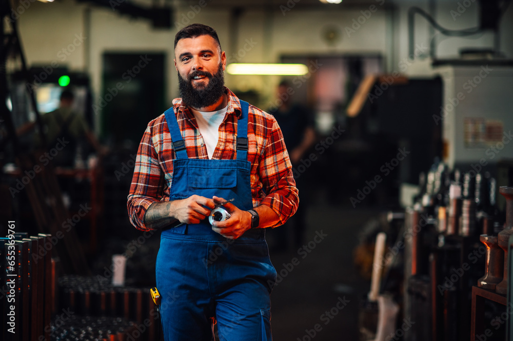 A portrait of a machinist holding a metal cylinder in a workshop. A portrait of a machinist holding a metal cylinder in a workshop.