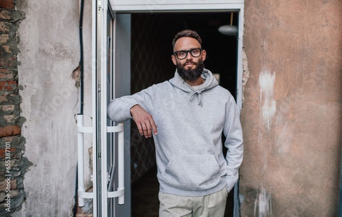 Urban Portrait of Handsome Hipster Man with a Beard Wearing a Gray Blank Hoodie with Space for your Logo or Design. Unique Mockup for Print