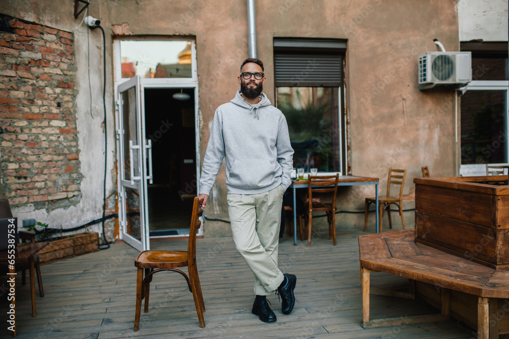 Fototapeta premium Urban Portrait of Handsome Hipster Man with a Beard Wearing a Gray Blank Hoodie with Space for your Logo or Design. Unique Mockup for Print