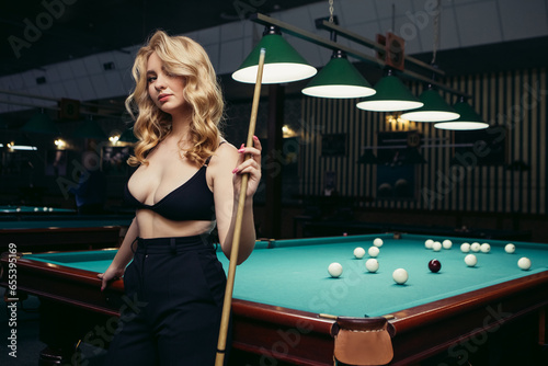 Blond woman playing enjoying billiard, hold cue, white billiard balls on table with green surface in billiard club. Pool game snooker pyramid player
 photo