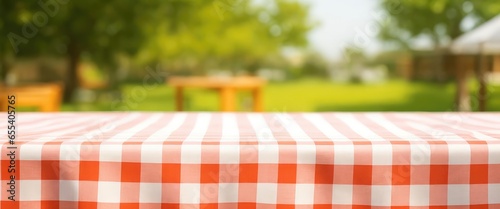 Product display, presentation. A tablecloth-covered, empty wooden deck table is in front of a blurry, green courtyard. Concepts of summer and picnic. Copy space for text, advertising, message, logo