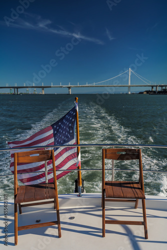 Chairs on the deck of a yacht crossing San Francisco Bay with American Flag and Bay Bridge in background