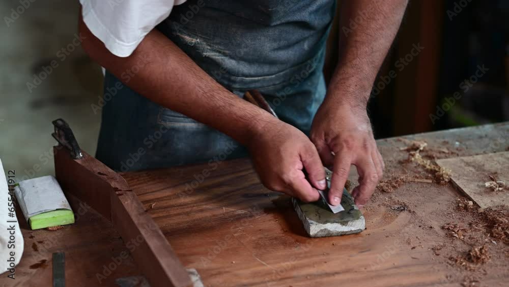 Woodworker is shown sharpening a chisel on a whetstone for making a classical guitar using tools in a traditional Woodworker is shown sharpening a chisel on a whetstone for making a classical guitar using tools in a traditional