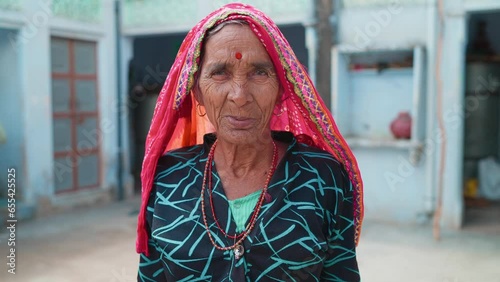 Close up shot of an Indian Hindu happy traditional Rural old woman or elderly female wearing colourful ethnic attire or saree standing outdoors looking at the camera. smiling