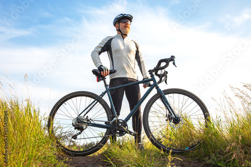 Bearded male cyclist is resting with a bike on the road in nature. cycling and health hobbies
