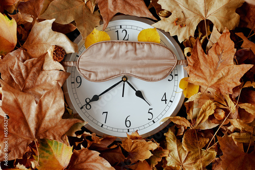 autumn background with clock, sleeping mask and leaves photo