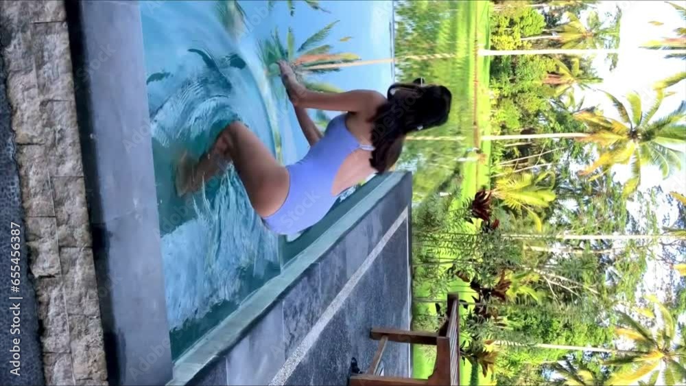 Beautiful woman jumps in water in swimming pool .l overlooking rice terraces and palms on Bali Island .Palms trees are reflected in the water. High vertical quality 4k footage