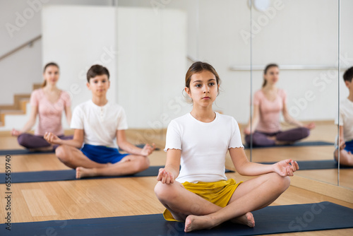 Young girl exercising lotus pose with her family during group yoga training.