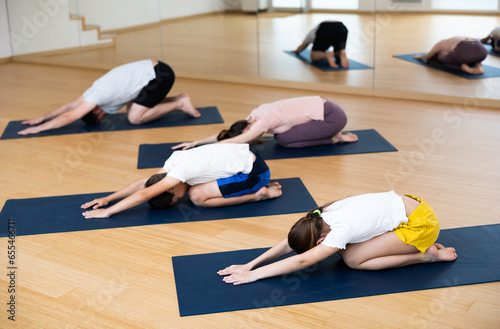 Kids and their parents lying on mats in child's pose during family yoga training.