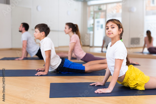 Positive pre-teen girl performing yoga exercises with brother and parents at gym, family health concept