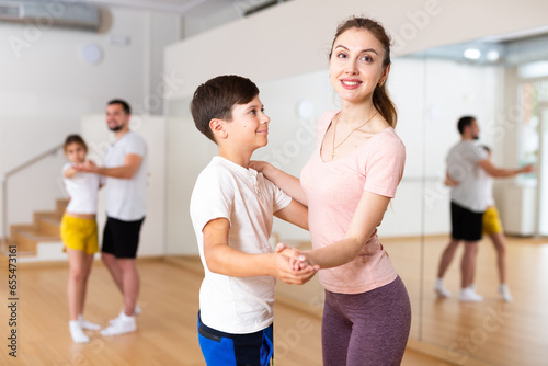 Smiling young woman dancing waltz in pair with her tween son during family dance class. Children and parents bonding time, active lifestyle concept