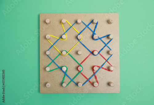 Wooden geoboard with rubber bands on green background, top view. Educational toy for motor skills development photo