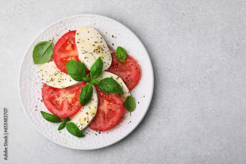 Plate of delicious Caprese salad with herbs on light grey table, top view. Space for text