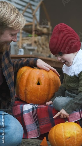 father and son carve eyes in pumpkin for halloween, vertical video