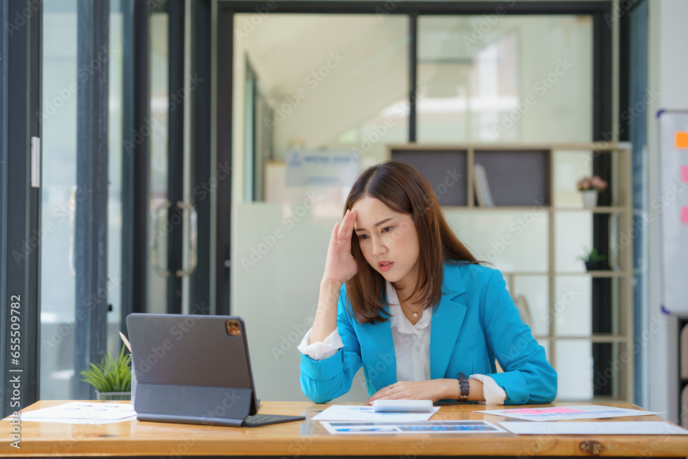 Portrait of an Asian Businesswoman sitting and working hard in front of a computer and lots of documents on the table in the workplace late with serious action, Work hard and too late concept. Portrait of an Asian Businesswoman sitting and working hard in front of a computer and lots of documents on the table in the workplace late with serious action, Work hard and too late concept.