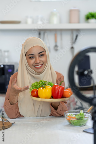 A young Muslim woman in a hijab prepares a vegetable salad and introduces fresh, colorful, useful vegetables. Making food menus while broadcasting live online with bloggers healthy food ideas.