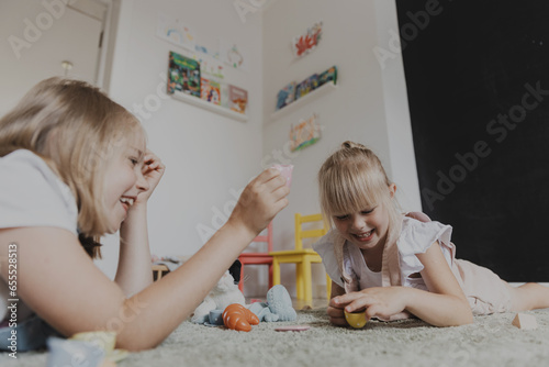 Close-up of female children playing with colorful toy kitchen play tea set. Kids sitting on carpet at bedroom or kindergarten, nursery. Educational eco game for child. Development of logical thinking