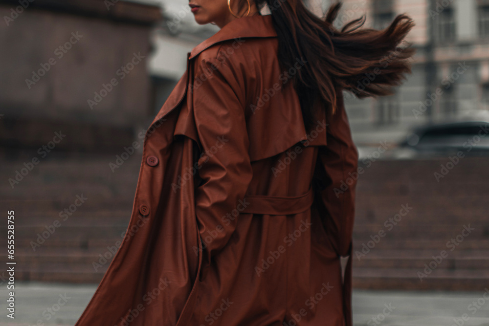 Fancy details of autumn long brown leather trench coat. Street style casual clothing. Woman walking alone in the city.