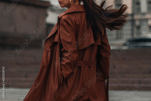 Fancy details of autumn long brown leather trench coat. Street style casual clothing. Woman walking alone in the city.