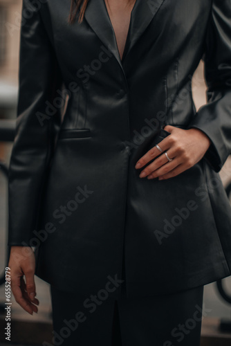 Fashion details of a black leather jacket with pockets and silver ring accessories on female hands. Fancy outfit, female accessories. Vertical