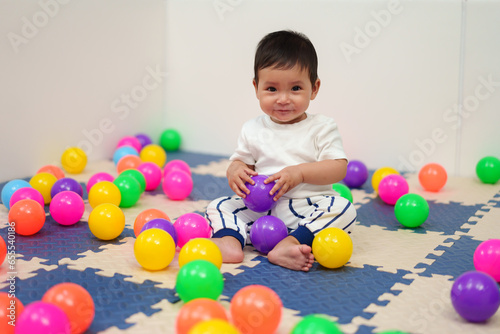 happy infant baby playing colorful balls in playpen