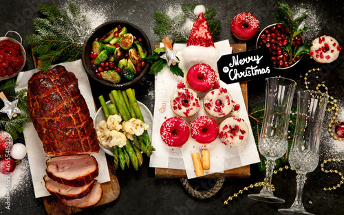 Baked ham with vegetablesand donuts on dark background. Christmas food photo