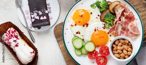 Traditional Englis breakfast plate with bacon strips, sunny side up eggs, vegetables and cake on light background photo