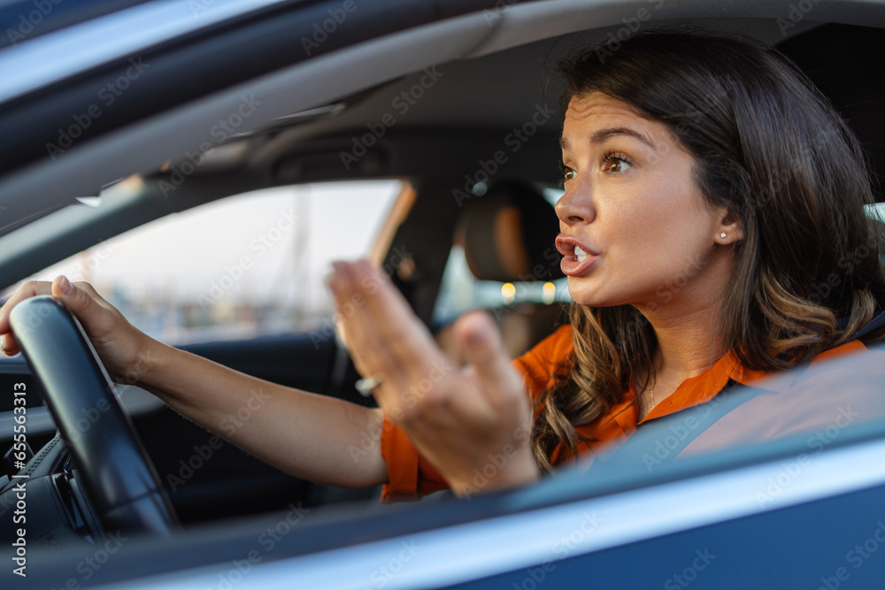 Closeup portrait, angry young sitting woman pissed off by drivers in front of her. Young woman sitting in a car stuck in a traffic jam feeling stressed because she is rushing to work.