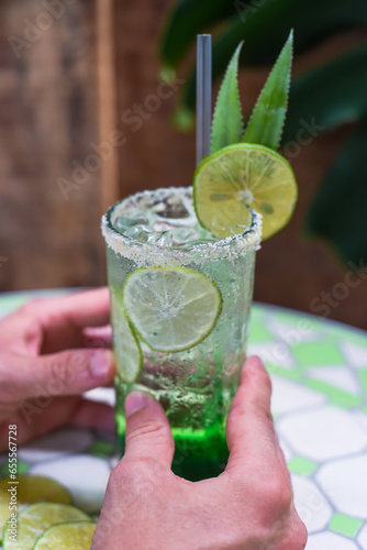 Hand holding panda leaves lemonade with desiccated coconut and green syrup on natural leaves background with copy space