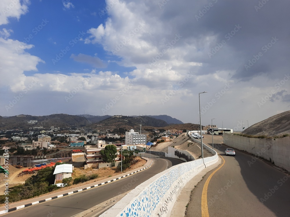 Beautiful daytime sky view of Al Bahah city in Saudi Arabia. City buildings, hills and clouds are visible in the background.