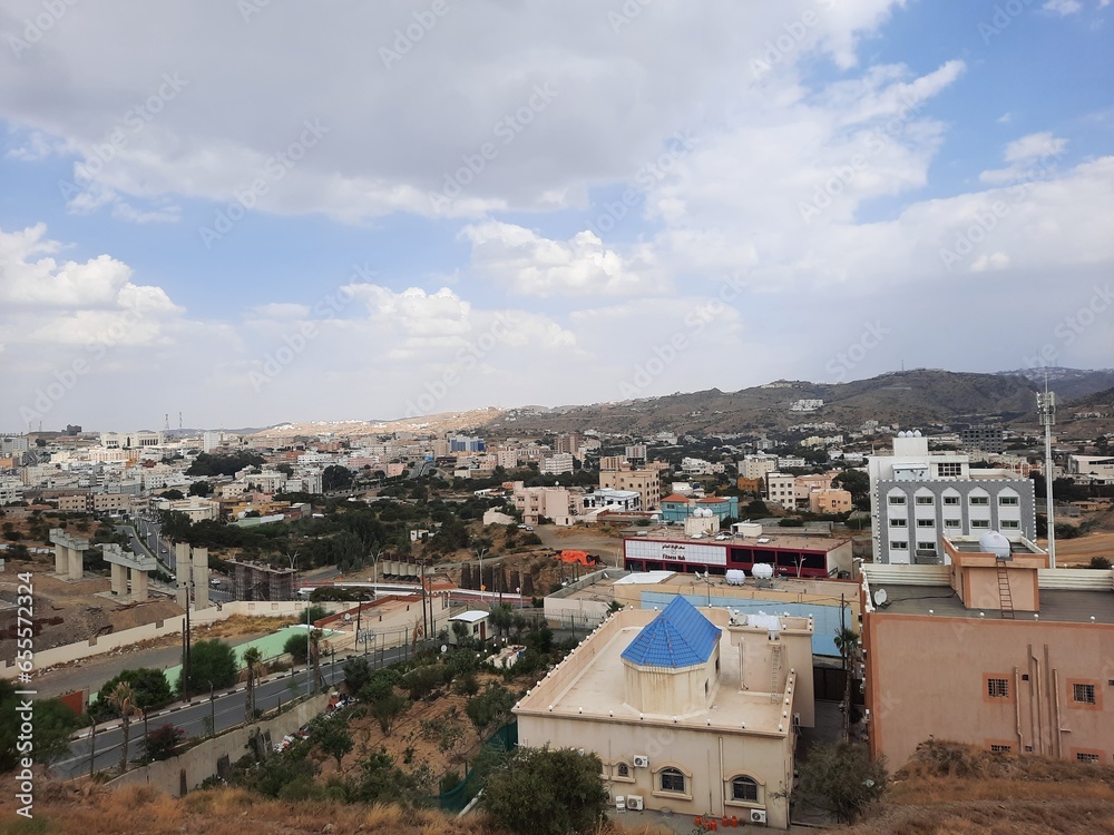 Beautiful daytime sky view of Al Bahah city in Saudi Arabia. City buildings, hills and clouds are visible in the background.