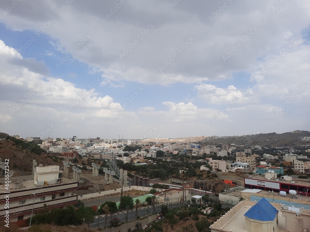 Beautiful daytime sky view of Al Bahah city in Saudi Arabia. City buildings, hills and clouds are visible in the background.