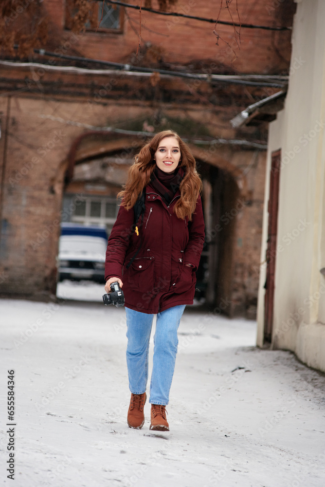Young redhead smiling girl with modern camera making photo in winter city