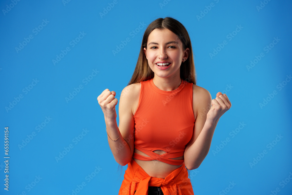 Portrait of a joyful happy teenage girl celebrating success on blue background Portrait of a joyful happy teenage girl celebrating success on blue background