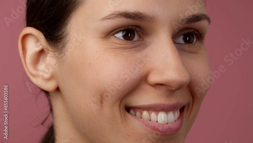 Closeup shot of young girl face with natural skin, no makeup, smiling with teeth. Looking away from camera.