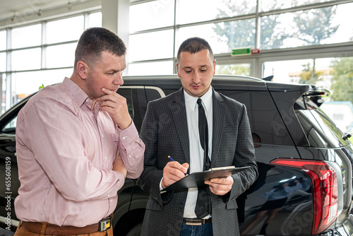 Caucasian salesman holding clipboard and talking about buying car with sale with his customer
