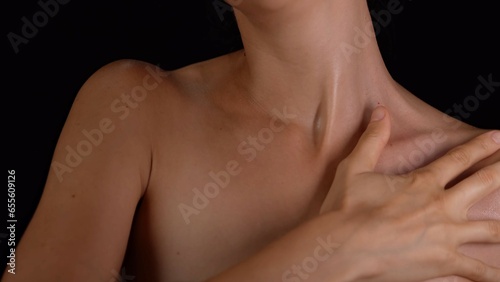 Closeup studio shot of shoulders and chest area body part, woman applying cosmetic product on her smooth skin.