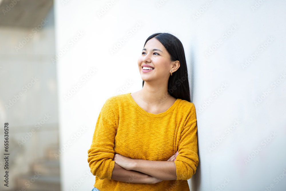 beautiful young smiling woman with arms crossed while leaning against wall beautiful young smiling woman with arms crossed while leaning against wall