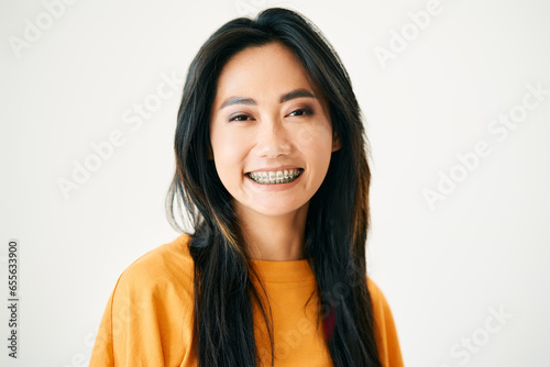 Closeup portrait of young smiling asian woman with braces on white studio background