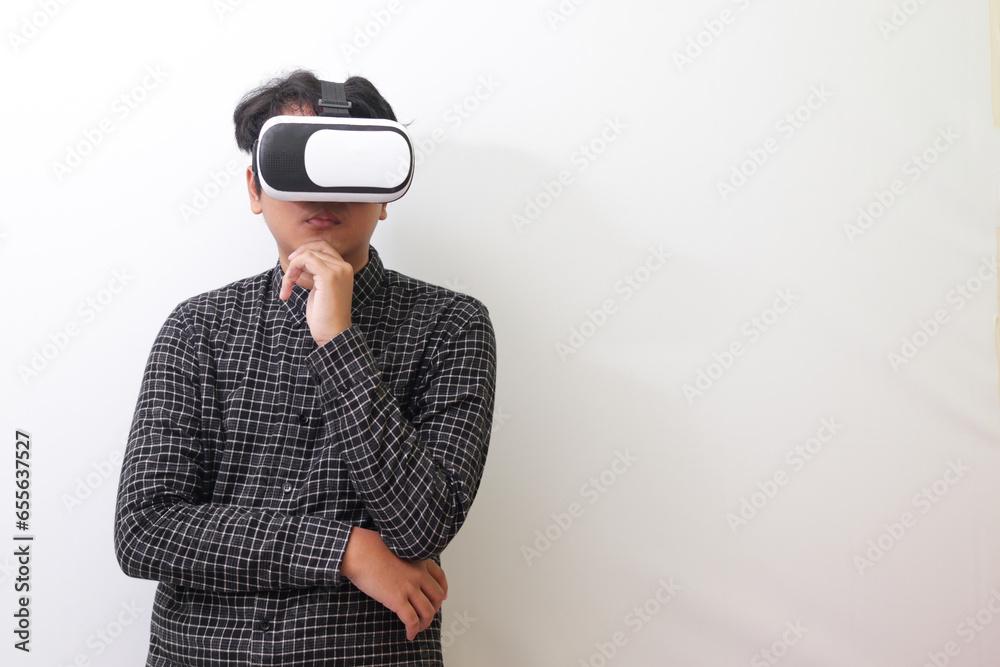 Portrait of Asian man in black plaid shirt using Virtual Reality (VR) glasses and thinking with hand on chin. Isolated image on white background Portrait of Asian man in black plaid shirt using Virtual Reality (VR) glasses and thinking with hand on chin. Isolated image on white background