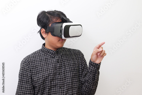 Portrait of Asian man in black plaid shirt using Virtual Reality (VR) glasses and trying to touch something in front of him. Isolated image on white background