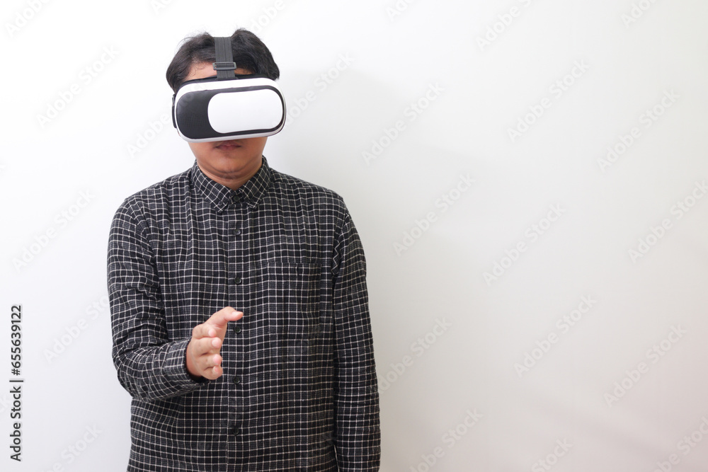 Portrait of Asian man in black plaid shirt using Virtual Reality (VR) glasses reaching out for a handshake and greet someone or his friend inside the game. Isolated image on white background Portrait of Asian man in black plaid shirt using Virtual Reality (VR) glasses reaching out for a handshake and greet someone or his friend inside the game. Isolated image on white background