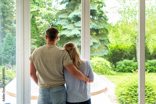 Tableau sur toile A couple standing at the window at home and looking out