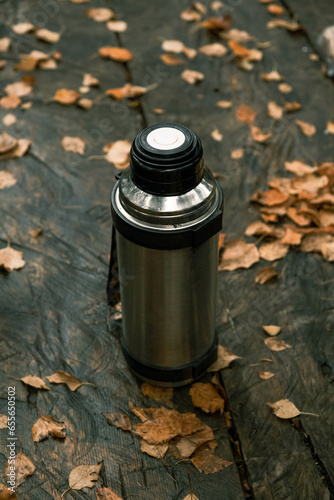 thermos with tea close-up on a wooden table in autumn in the forest 