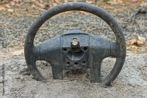 Automobile old discarded dirty black rubber industrial broken round modern steering wheel lies in the sand in the forest in nature during the day