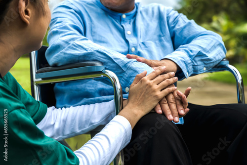 Care taker woman holding hands man in wheelchair to encourage