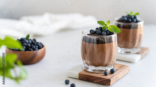 Vegan chocolate mousse in glasses decorated with fresh blueberry and mint on a marble board on a white concrete background. Close up. Protein diet recipe. Creamy chocolate yogurt, panna cotta dessert