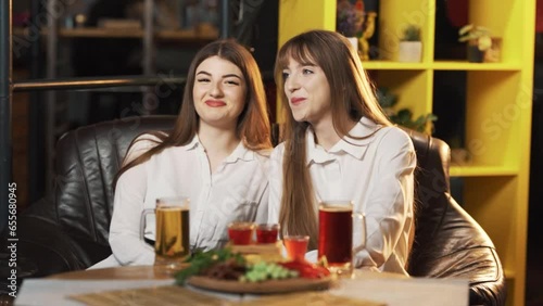 Two beautiful girls in a bar at a table are looking at guys and flirting and courting photo