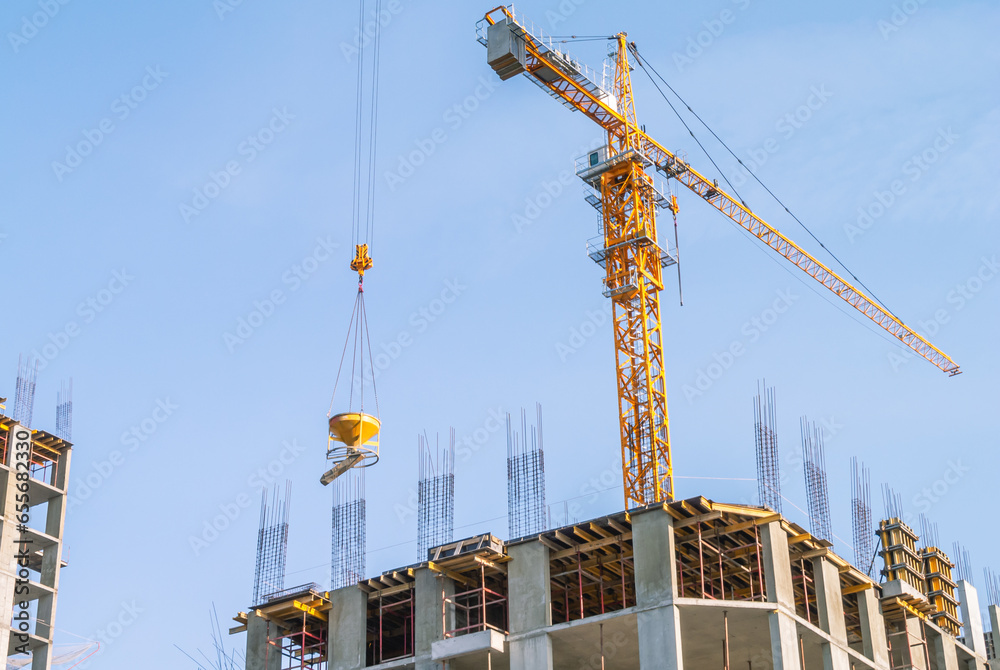 Orange crane on a blue sky background. Equipment for the construction and lifting of bulky loads during the construction of buildings. A tower crane lifts a bucket of cement mortar.